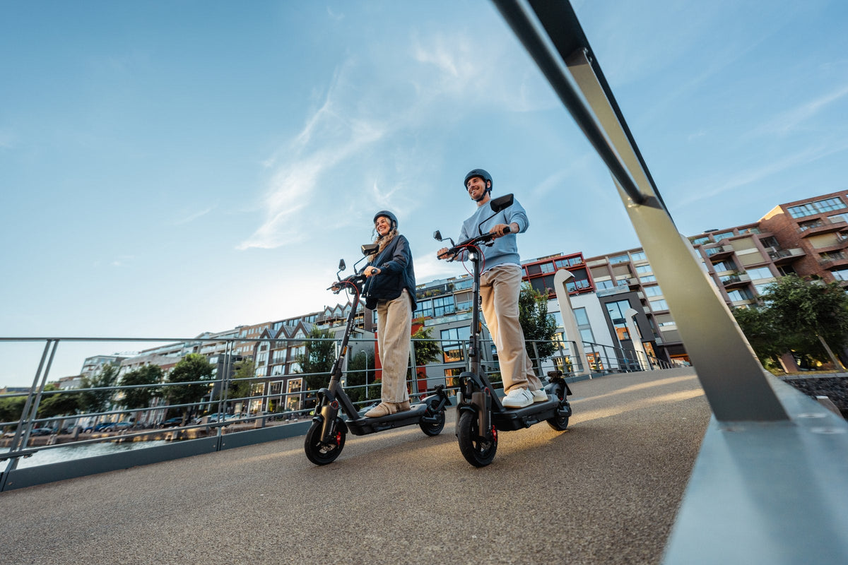Man en vrouw rijden op de Segway Ninebot Max G3 NL elektrische step over een brug in een Nederlandse stad